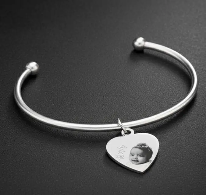 Pulsera estilo bangle rigida abierta -con/dije ac. Inox. Pleateada